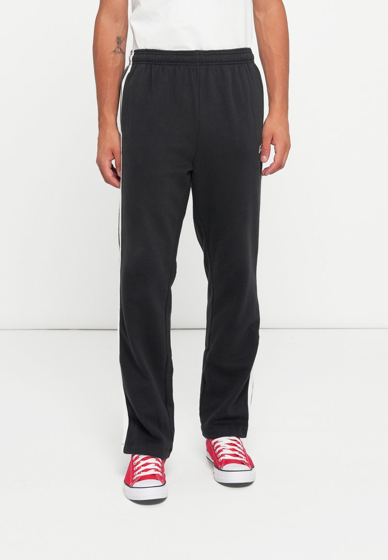 Black sweatpants made of soft fabric, featuring a relaxed fit, elastic waistband, and white side stripes, paired with red sneakers.