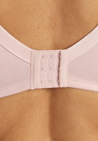 Rückansicht einer Person, die einen hellrosa BH mit einem dreifachen Haken- und Ösenverschluss direkt auf der Haut trägt.