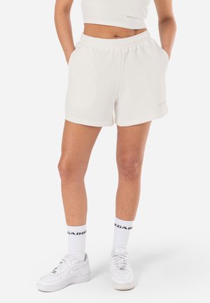 Pantalones cortos blancos de canalé con una cinturilla elástica y bolsillos laterales. Combinados con zapatillas blancas y calcetines blancos con letras negras.