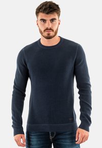 Maglione in maglia a costine blu navy con scollatura rotonda, maniche lunghe e tessuto testurizzato, caratterizzato da un'etichetta discreta sull'orlo e un design aderente.