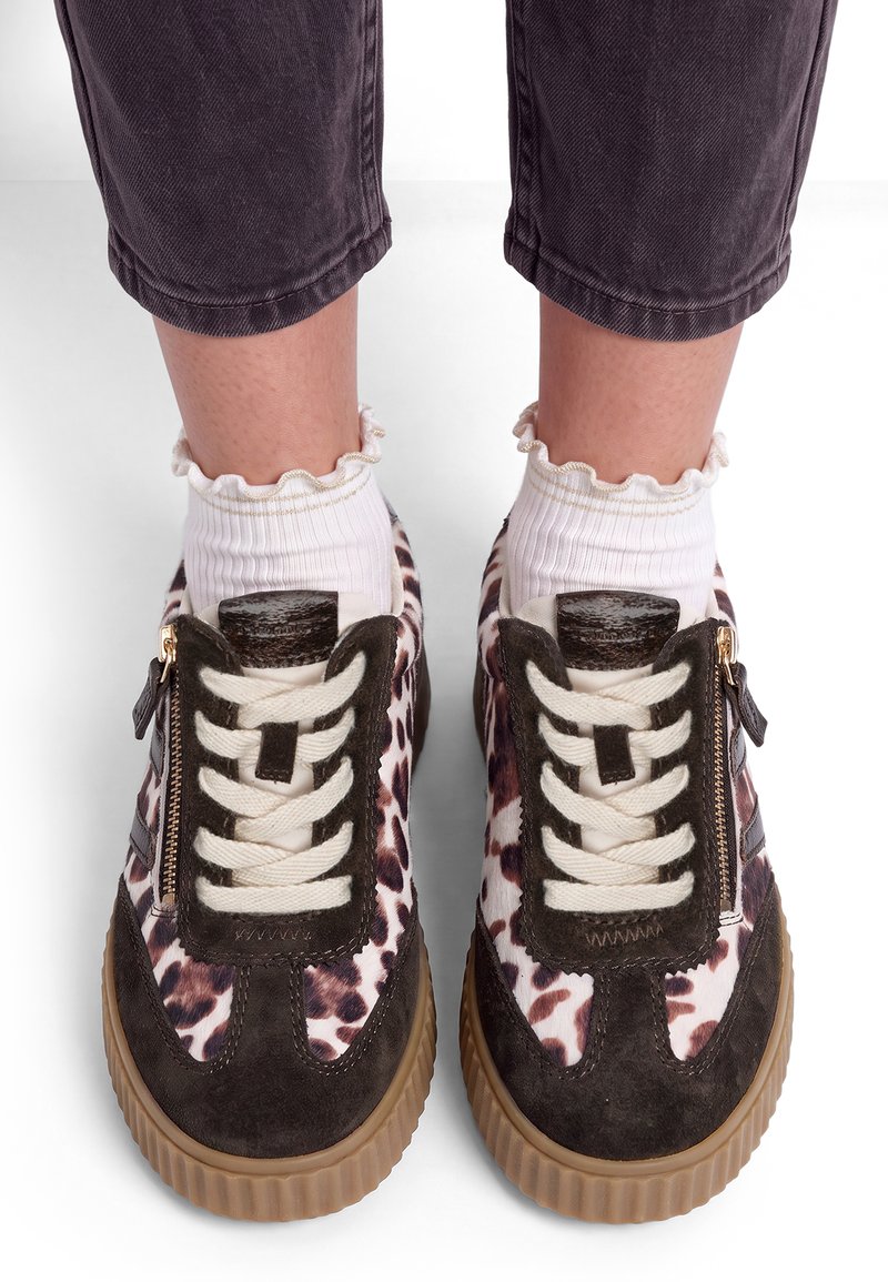 Πόδια με λευκές ankle socks με βολάν και μαύρα, λευκά και καφέ sneakers με λεοπάρ σχέδιο, κορδόνια μπροστά και χρυσά φερμουάρ στο πλάι.