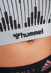 Cinturilla deportiva gris acanalada con líneas verticales negras y logotipo "hummel"; textura suave visible contra la piel.