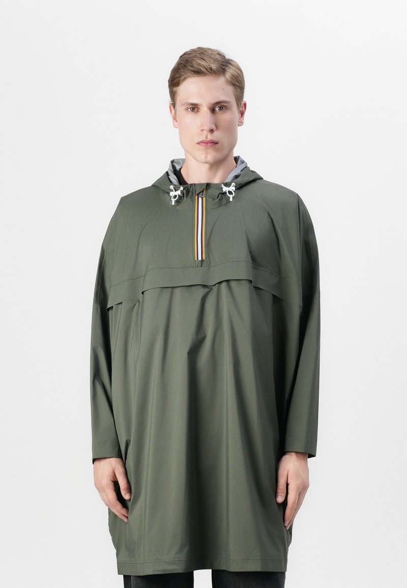 Grön vattentät huvad poncho med en fjärdedelsdragkedja och flerfärgad rand. Löst sittande, med långa ärmar och subtil textur.