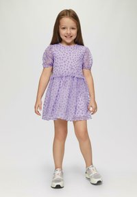 Lila Kleid mit Puffärmeln, strukturiertem Punktmuster und Schichtenrock. Kombiniert mit weißen und grauen Sportschuhen. Glattes Material.