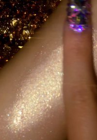 Shimmering golden sequins and a sparkling, iridescent finger highlight a smooth, luminous skin surface with a fine glitter texture.