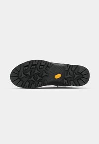 Black rubber shoe sole with prominent tread pattern. Features yellow Vibram logo and textured areas for grip and stability.