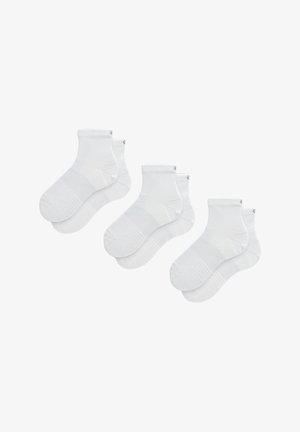 Calzini bianchi alla caviglia realizzati in un materiale morbido e elasticizzato, con un bordo a coste e una suola texturizzata per una maggiore aderenza. Visibili quattro paia.