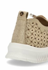 Zapatilla slip-on beige con patrón perforado, acentos metálicos y suela de goma blanca. Cuenta con un cierre de cremallera y un panel trasero texturizado.