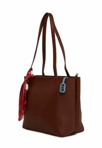 Brūna teksturēta ādas somiņa ar divām pleca siksnām, ko rotā sarkans rakstains šalle un zils uzlīmes tagiņš uz rāvējslēdzēja.