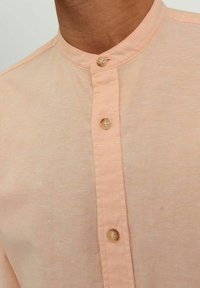 Camicia collare rosa chiaro con un tessuto testurizzato e cinque bottoni visibili, caratterizzata da uno stile colletto alla cinese e semplici dettagli di cucitura.