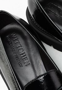 Scarpe in pelle verniciata nera con una finitura liscia e lucida. Presentano un'etichetta impressa "WITTCHEN" e una cucitura lungo il bordo.
