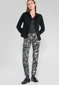 Zwarte denimjas met knoopsluiting, grijze top en gemonteerd crèmekleurige en zwarte broek. Outfit compleet met zwarte instappers en grijze sokken.