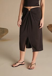 Jupe mi-longue noire en tissu doux, dotée d'un design avant twisté avec une découpe circulaire et une fente avant pour faciliter le mouvement.