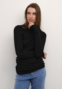 Maglione a maniche lunghe nero con collo alto realizzato in un morbido tessuto leggero; design aderente con una consistenza liscia, abbinato a jeans azzurri chiari.