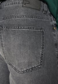 Jeans in denim grigio con una texture morbida, dotati di una tasca posteriore, dettagli cuciti e una patch in pelle nera sulla vita.