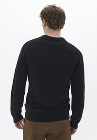 Suéter de punto ribeteado negro con rayas horizontales, cuello redondo y mangas largas, combinado con pantalones marrones texturizados.