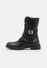 Černá kožená vojenská bota do poloviny lýtek se postranním popruhem s přezkou, předními šněrováním a silnou gumovou podrážkou na jednoduchém bílém pozadí.