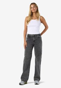 Ljust grå vida jeans med en urtvättad finish, kombinerat med en figurnära vit ribbad linne. Outfiten har avslappnade träningsskor.