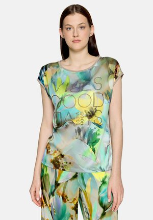 Jonge vrouw draagt een kleurrijke, met bloemen bedrukt topje en bijpassende broek met de tekst "Vibes, Good Days" op het shirt.