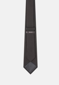 Cravate à motif foncé avec un tissu texturé présentant de petites formes de diamant. Comprend une boucle de fixation et une pointe lisse, unie et noire.