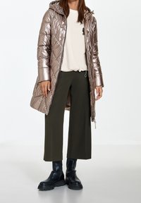 Metallic rosegold pufferjakke med hætte, med et quiltet design. Blevet parret med en off-white top og olivengrønne vidde bukser, afsluttet med sorte støvler.