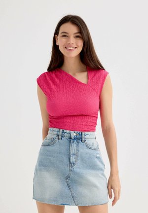 Top ajustado de textura rosa con mangas cortas y escote diagonal, combinado con una falda mini de mezclilla azul claro con dobladillo deshilachado.