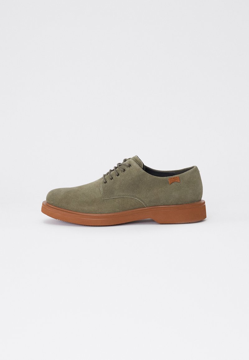 Pantofi din suede verde, cu șireturi, cu vârful rotunjit, având o talpă din cauciuc maro și detalii minime de coasere. Nu există branduri vizibile.