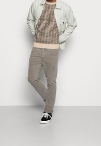 Szare spodnie o wąskim kroju, jasnoszara koszula-kurtka oraz wzorzysty brązowy sweter z prążkowanym dołem. Czarne sneakersy z białymi podeszwami.