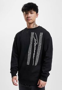 Black sweatshirt featuring a distinct white graphic with text and "Roamer" printed vertically. It has a round neck and long sleeves.