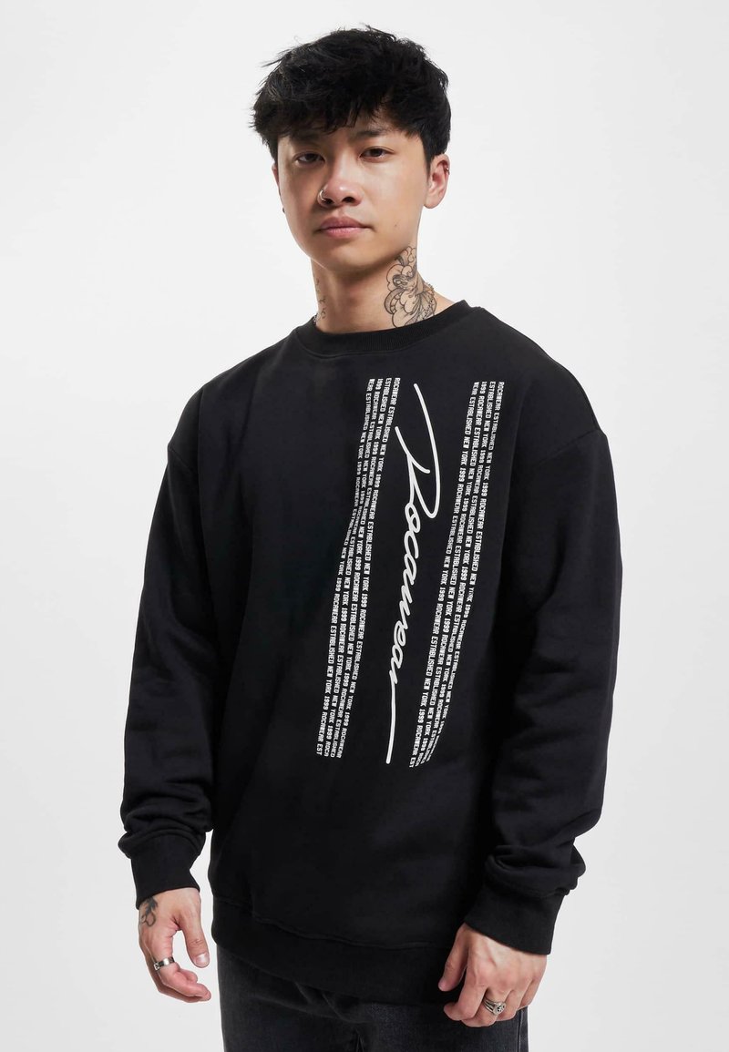 Black sweatshirt featuring a distinct white graphic with text and "Roamer" printed vertically. It has a round neck and long sleeves.