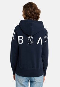 Námornícka mikina s kapucňou na šnúrku, so širokými bielymi písmenami "LBSAN" na chrbte. Mäkká tkanina s rebrovanými manžetami a lemom.