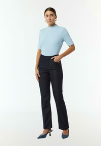 Jasnoniebieski prążkowany top z krótkim rękawem, w zestawieniu z ciemnoniebieskimi jeansami prostymi. Modelka nosi niebieskie czółenka na szpilce, stoi z jedną ręką na biodrze.