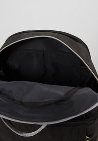 Intérieur de sac à dos noir avec un tissu lisse et mat, fermeture éclair, et doublure grise. Comprend un compartiment rembourré et sans motifs visibles.