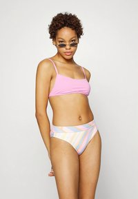 Top de biquíni cor-de-rosa com alças finas combinado com cuecas de cintura alta com riscas multicoloridas em tons pastel. Tecido macio, design ajustado.