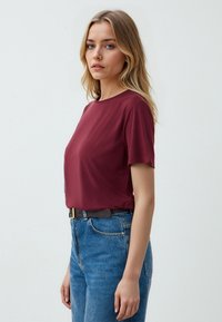 T-shirt bordeaux a girocollo e maniche corte, abbinato a jeans in denim blu a vita alta. Tessuto morbido e design semplice.