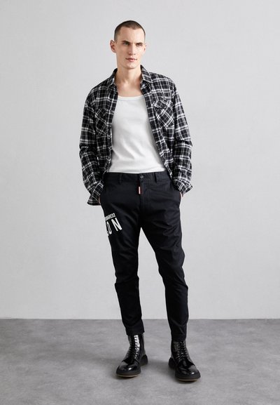 Black plaid shirt over a white tank top, paired with black tapered pants featuring a white print, completed with black lace-up boots.