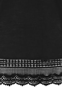 Schwarzer Stoff mit einer strukturierten Oberfläche zeigt einen detaillierten Spitzenabschluss, der runde Akzente und eine gewellte Kante umfasst und so einen geschichteten Look erzeugt.