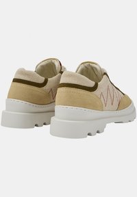 Beige suede and canvas shoes with white rubber sole, featuring red zigzag stitching and green accents. Rounded toe, low-top design.