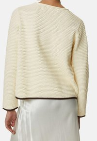 Sweter w kolorze kremowym z teksturowanym, wafelowym splotem, brązowymi wykończeniami przy dekolcie i mankietach oraz luźnym krojem.