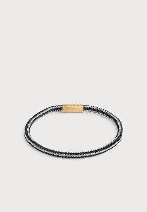 Bracelet tressé noir et argent avec un fermoir cylindrique en or orné de motifs géométriques gravés.