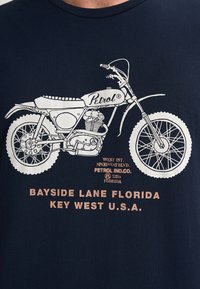 Tmavě modré tričko s bílou grafikou motocyklu a nápisem "Petrol" a textem "BAYSIDE LANE FLORIDA KEY WEST U.S.A."