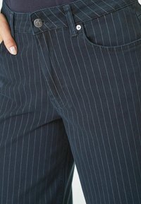 Dunkelblaue Jeanshose mit dünnen vertikalen Streifen, vorderen Taschen, Metallknopfverschluss und dezenten Stickdetails.