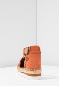Espadrilles in camoscio arancione con design floreale intagliato, cinturino in pelle marrone chiuso con una fibbia dorata e suola in corda di juta.