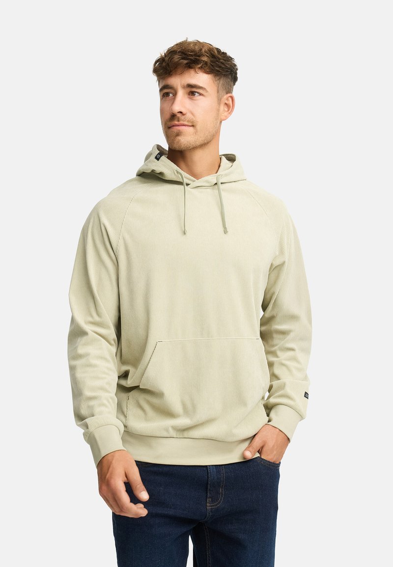 Lys grøn hoodie lavet af tekstureret stof, med en frontlomme, justerbare snore og ribbede cuffs. Paret med mørke jeans.