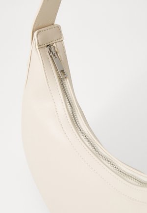 Gros plan d'une fermeture éclair d'un sac en cuir beige avec des coutures visibles et une surface lisse et courbe sur un fond clair.