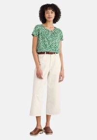 Blusa verde a maniche corte con motivo floreale bianco, pantaloni beige a gamba larga e zoccoli marroni con tacco in legno.