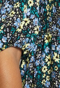 Mustavalla kukkakangas, jossa on sinisiä ja keltaisia kukkia, teksturoitu pinta ja rypistetty hiusdetail. Suora käsi osittain näkyvissä.