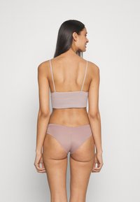 Soutien-gorge de sport mauve avec des fines bretelles et un design sans couture, associé à un bas de bikini taille basse assorti, tous deux fabriqués en tissu lisse.