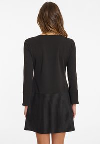 Knieumhangkleid mit schwarzem Oberteil und gestreiftem Rock. Hergestellt aus weichem Stoff mit langen Ärmeln und rundem Halsausschnitt.