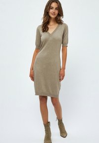Robe en tricot couleur marron clair avec un décolleté en V et des manches courtes, silhouette ajustée et ourlet côtelé, associée à des bottines.